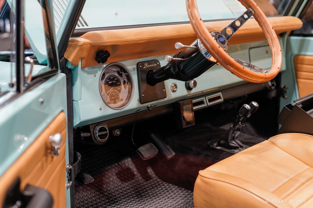 Close-up of a vintage Ford Bronco interior featuring a mint green dashboard, tan leather upholstery, and a classic steering wheel.